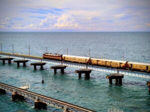 A train travels across a long bridge over the ocean under a blue sky with clouds.